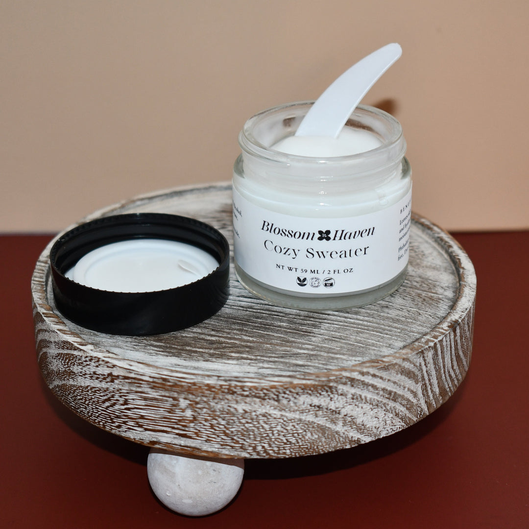 Jar of 'Cozy Sweater' candle with a spoon on a wooden stand against a beige background