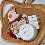 A curated fall-themed gift set arranged in a carved wooden tray. The set includes a round white jar labeled 'Pumpkin Latte' by Blossom & Harvey, a small bottle, a die-cut 'Fall Sweet' card, and a clear packet labeled 'Pumpkin Latte' by the same brand, all on a light neutral background.