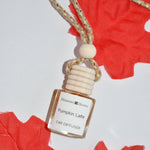 A small car diffuser bottle labeled 'Pumpkin Latte' by Relaxing Aroma, featuring a cream-colored wooden cap and a braided rope, styled on a white background with red maple leaves.