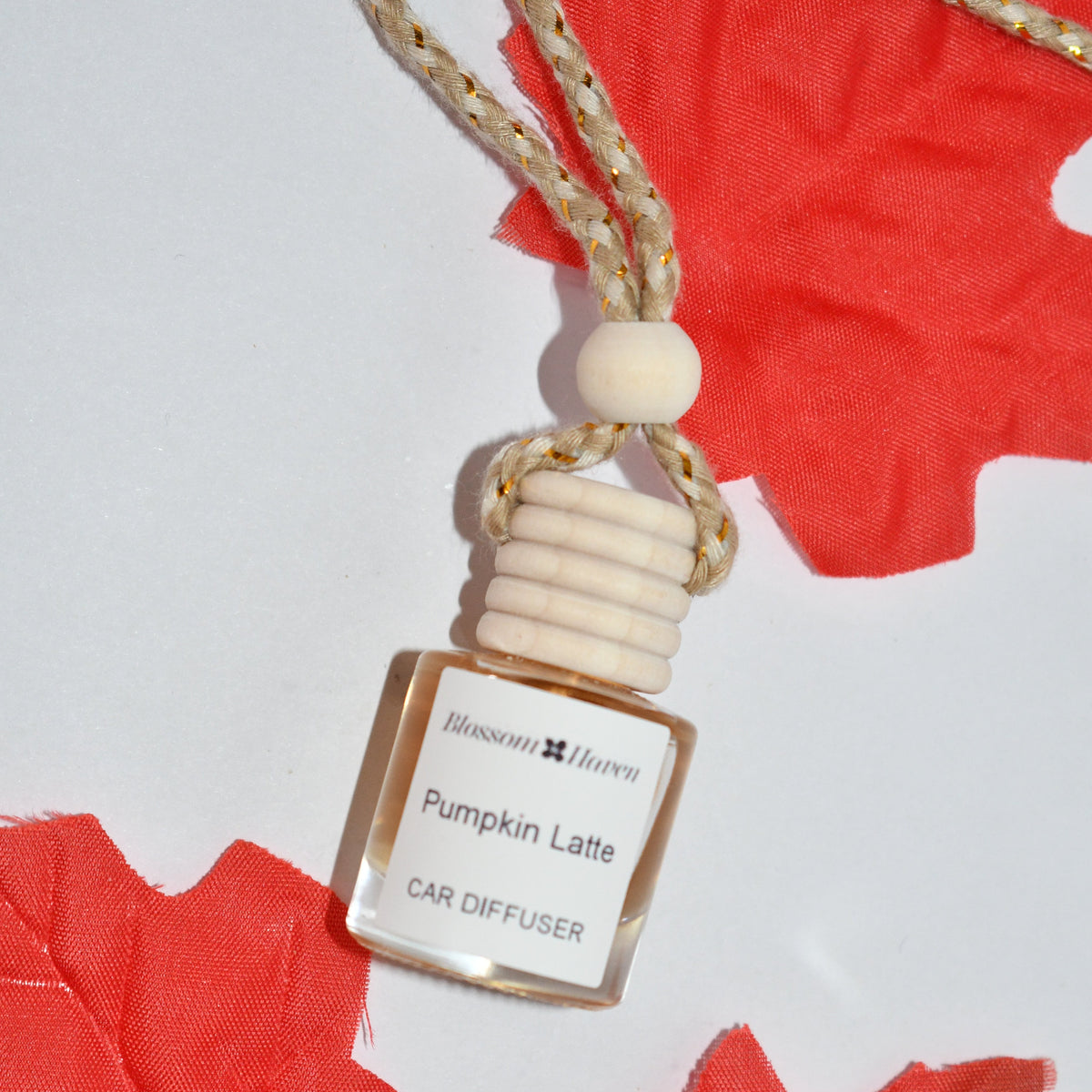 A small car diffuser bottle labeled 'Pumpkin Latte' by Relaxing Aroma, featuring a cream-colored wooden cap and a braided rope, styled on a white background with red maple leaves.