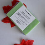 A rectangular bar of light green soap wrapped in clear plastic with a white label reading 'Apple Harvest,' placed on a white surface with red maple leaf props.