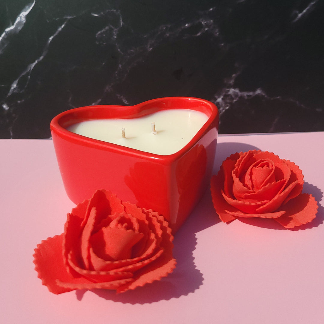 Red heart-shaped candle with floral design on a black and pink marble surface