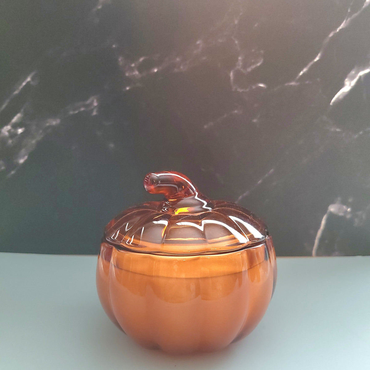 Amber-colored glass container with a lid on a light surface with a dark marble background