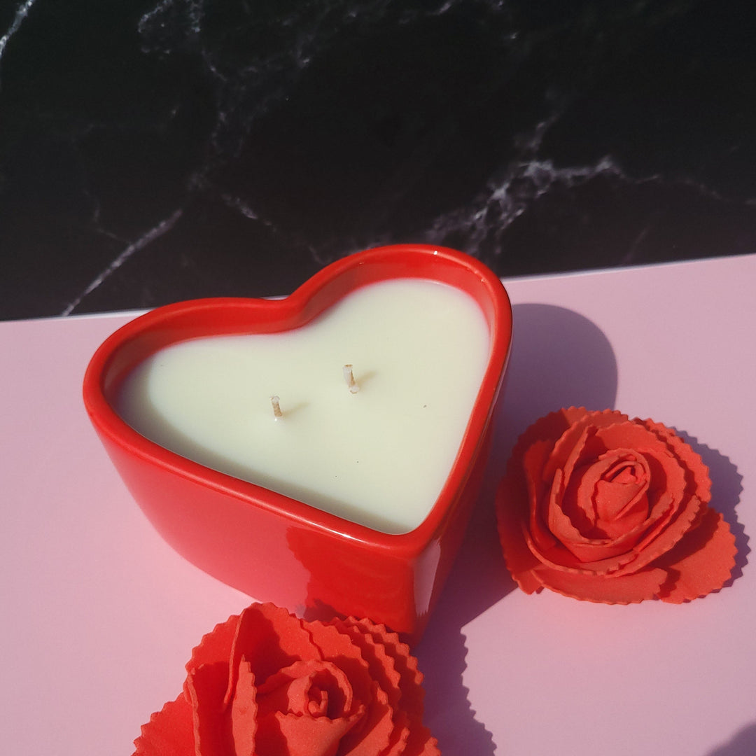 Heart-shaped candle with red floral decorations on a black and pink background