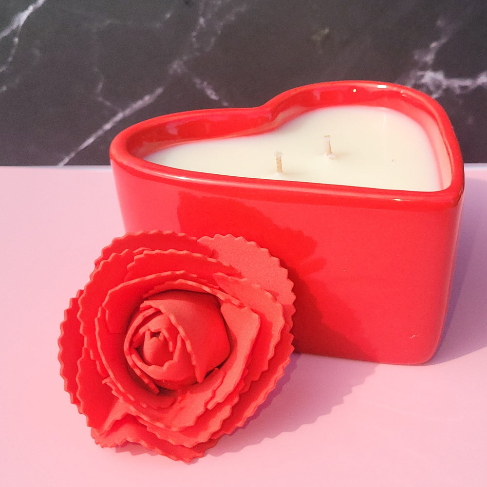 Red heart-shaped container with a white candle and a red rose on a pink and black marble background