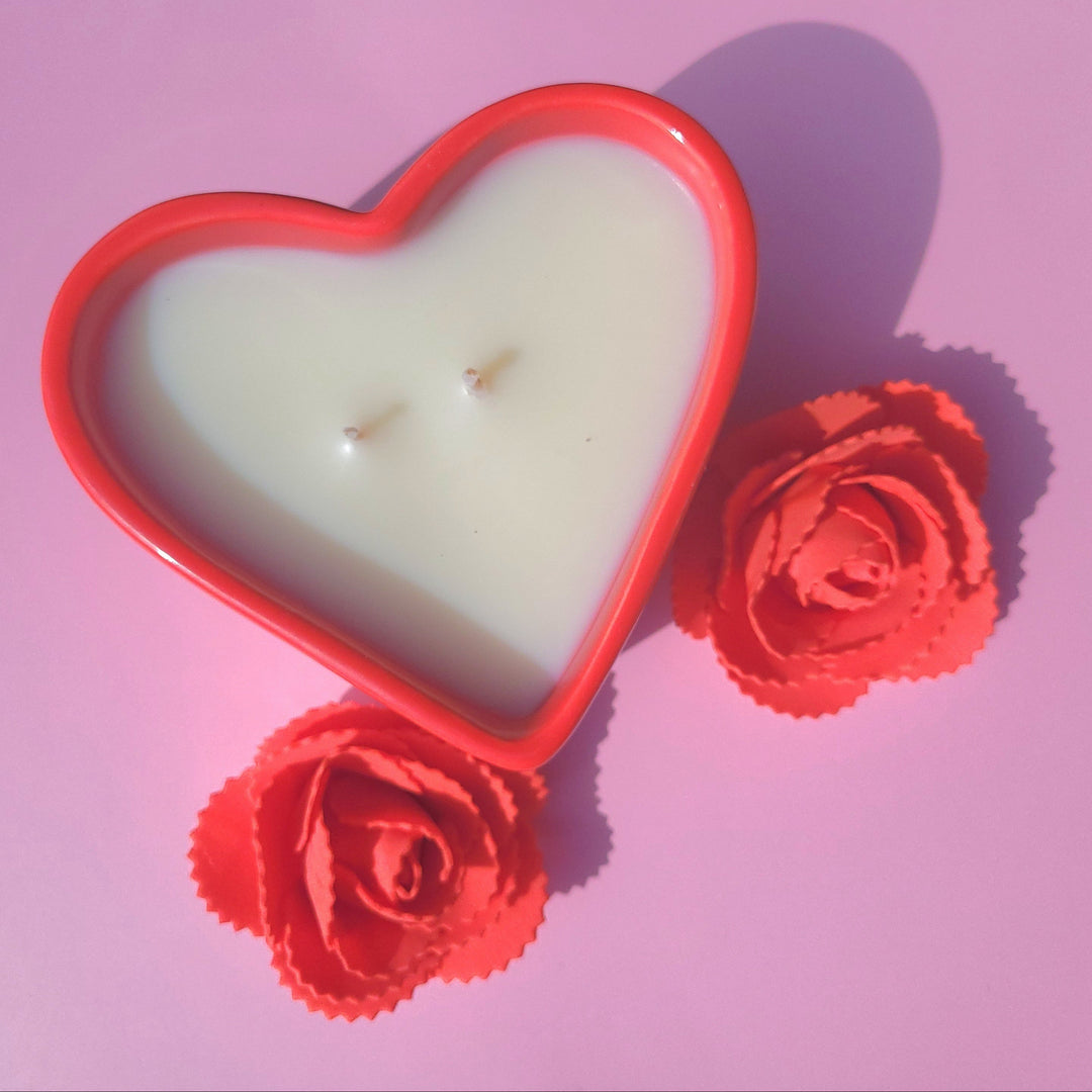 Heart-shaped candle with red floral decorations on a pink background