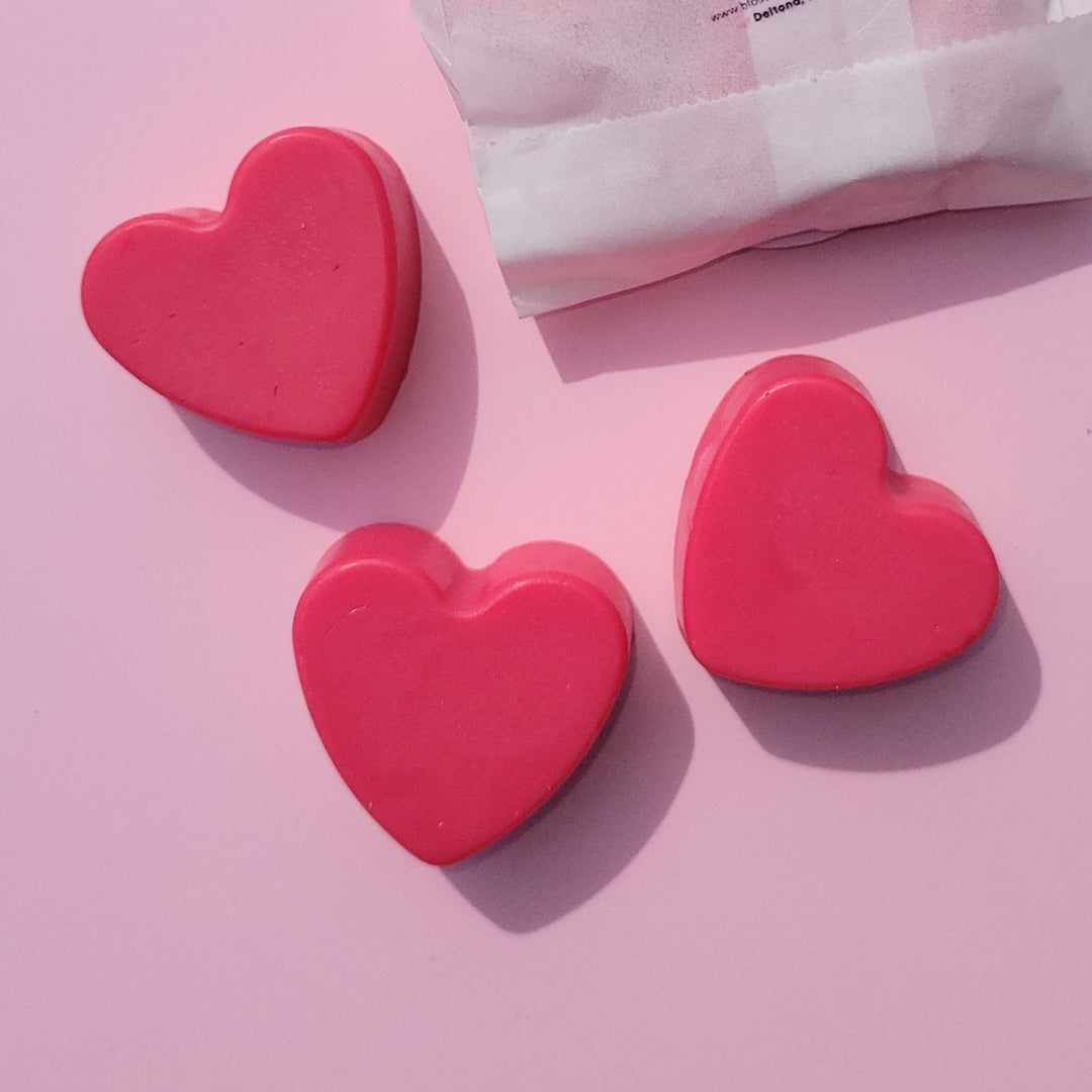Pink heart-shaped soaps and a white packet on a pink background