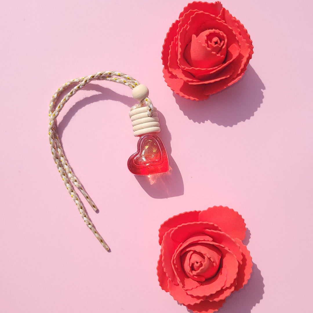 Red heart-shaped car diffuser with two red roses on a pink background.