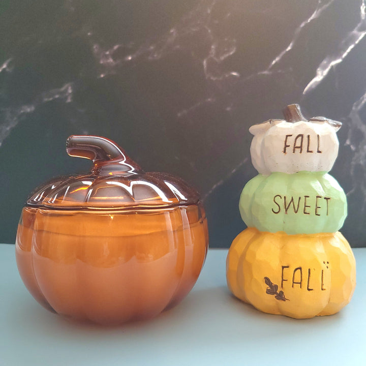 Pumpkin-shaped containers with a lid and stacked pumpkins on a marble surface