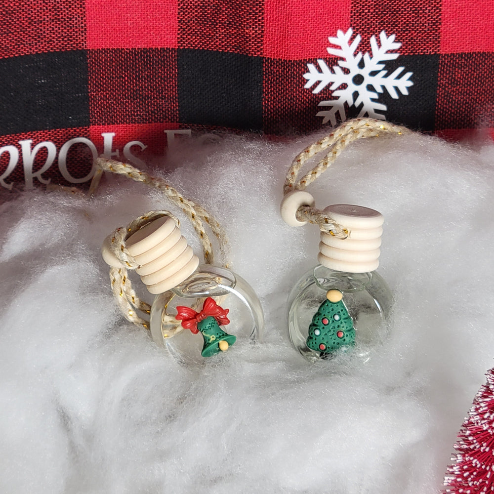 Decorative bottle charms with Christmas trees on a red and black checkered fabric background.